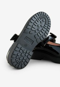 Zwarte gepatineerde leren schoen met een chunky zool. Voorzien van een gestructureerd profiel, verstelbare gesp en "BAKER" branding aan de onderkant.