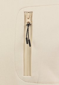 Tessuto beige con superficie texturizzata presenta una zip laterale con un tirante fluido e dettagli con cordini neri.