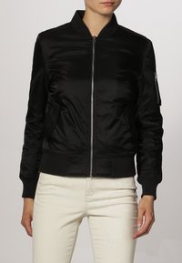 Blouson bomber en satin noir avec fermeture éclair à l'avant, poignets et ourlet côtelés. Comprend des poches latérales et une poche zippée sur la manche pour le rangement.
