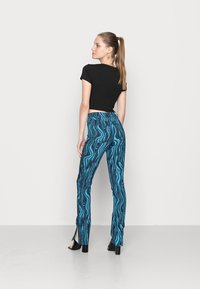 T-shirt preto curto combinado com calças flare azuis com padrões de ondas, fendas nas bainhas e sapatos de salto alto pretos.