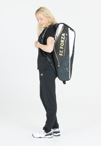 Svart och vit sportväska med guldtryck, som har en elegant design, böjd form, texturerade detaljer och justerbara remmar.