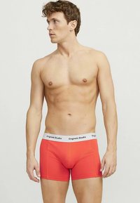 Røde boksershorts med hvit "Originals Studio" midjebånd, tettsittende design, glatt tekstur og korte ben, som viser et ensfarget mønster.