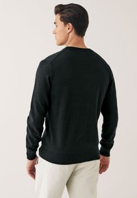 Suéter negro de punto, con cuello redondo, puños y dobladillo acanalados, silueta ajustada, textura suave, usado con pantalones de color claro.