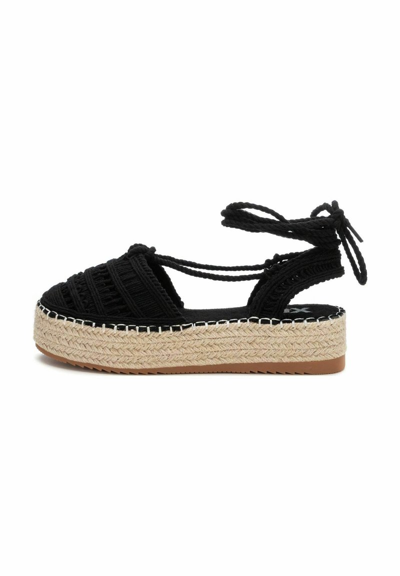 Sandal de esparto tejido negro con una gruesa plataforma de yute y lazos en el tobillo. Presenta una parte superior texturizada y costuras blancas en contraste a lo largo de la suela.