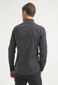 Camicia nera con bottoni, caratterizzata da un piccolo motivo a pois bianchi, con colletto classico e maniche lunghe, realizzata in tessuto leggero.