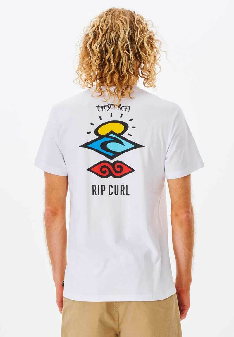 Camiseta de manga corta blanca con un gráfico colorido en la parte posterior que presenta un sol, una ola y patrones en espiral; incluye el texto "THE SEARCH" y "RIP CURL".