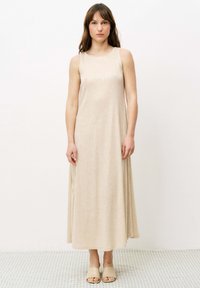 Ärmelloses beiges Maxikleid aus einem glatten, leicht strukturierten Stoff, mit Rundhalsausschnitt und fließender Silhouette, ergänzt durch neutrale Sandalen.