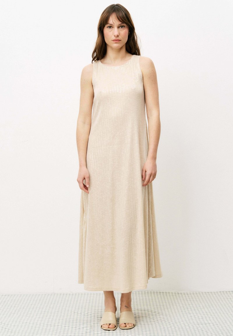 Ärmelloses beiges Maxikleid aus einem glatten, leicht strukturierten Stoff, mit Rundhalsausschnitt und fließender Silhouette, ergänzt durch neutrale Sandalen.