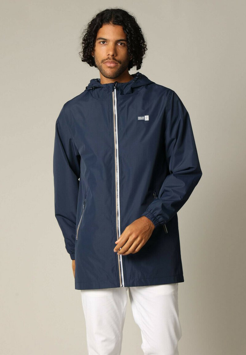 Veste imperméable marine avec fermeture éclair à l'avant, capuche ajustable, poignets élastiques et poches latérales ; fabriquée à partir d'un matériau léger et lisse.