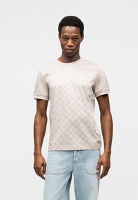 Ανοιχτό μπεζ κοντομάνικο μπλουζάκι με υφασμάτινο σχέδιο, στρογγυλή λαιμόκοψη και μαλακό βαμβακερό υλικό. Συνδυασμένο με τζιν παντελόνι ανοιχτού χρώματος.