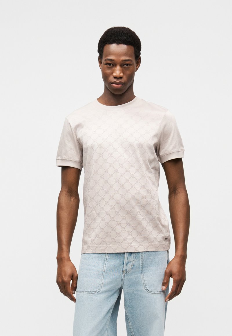 Ανοιχτό μπεζ κοντομάνικο μπλουζάκι με υφασμάτινο σχέδιο, στρογγυλή λαιμόκοψη και μαλακό βαμβακερό υλικό. Συνδυασμένο με τζιν παντελόνι ανοιχτού χρώματος.