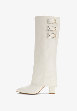 Botte blanche en cuir, hauteur genou, avec un bout pointu, trois accents de boucles métalliques et un talon carré bloc. Texture lisse, design minimal.