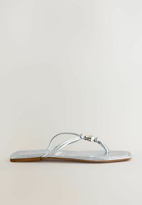 Sandale plate argentée avec des lanières fines, un bout carré et une petite boucle métallique sur une semelle marron clair.