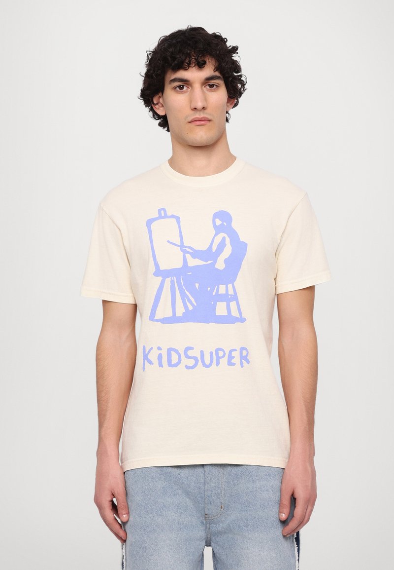 Cremefarbendes Baumwoll-T-Shirt mit einer blauen künstlerischen Grafik eines Figuren, die auf einem Malstock malt, und dem Text "KIDSUPER" am unteren Rand.