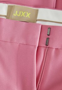 Roze stoffen broek met een gladde textuur, voorzien van een contrasterende witte tailleband en een gouden logo, metalen hardware-accenten en een rits.