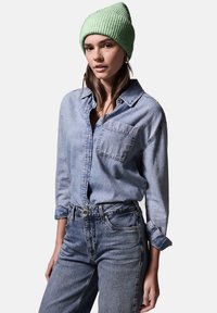 Lichtblauwe denim shirt met lange mouwen en een borstzak, gecombineerd met hoge taille blauwe jeans en een muntgroene geribde beanie.