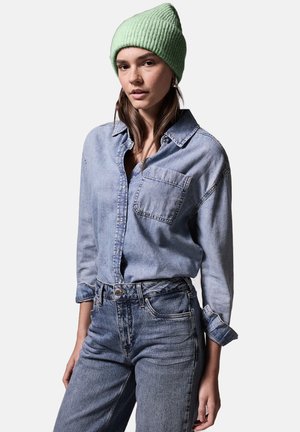 Lichtblauwe denim shirt met lange mouwen en een borstzak, gecombineerd met hoge taille blauwe jeans en een muntgroene geribde beanie.