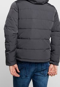 Graue Stepp-Wattierte Jacke mit horizontalen Nähten, Kapuze und elastischen Bündchen. Trägt man über blauen Jeans und zeigt ein lässiges, isoliertes Design.