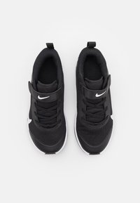 Black athletic shoes with a textured fabric upper, laces, and a Velcro strap. Features a white Nike logo and contrasting white outsole.