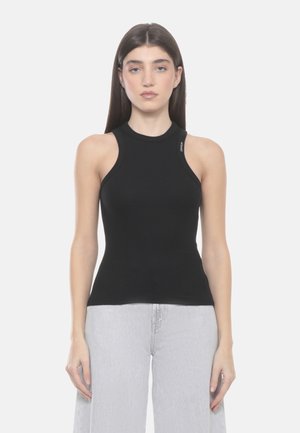 Giovane donna con capelli castani lisci che indossa un top nero senza maniche a coste e pantaloni grigio chiaro a vita alta e gamba larga.