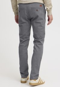Pantalones de algodón grises con un corte recto, dos bolsillos traseros, detalles en botón marrón y un pequeño parche con logo. Combinados con zapatillas crema.