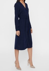 Abito lungo blu navy con maniche lunghe, apertura frontale con bottoni, vita cintrata e colletto, realizzato in tessuto leggero, lunghezza al ginocchio e vestibilità rilassata.