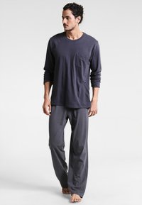 Navyblaues Langarmshirt mit Tasche, kombiniert mit lockeren, gemusterten Schlafanzughosen mit weißen Punkten auf dunklem Hintergrund.