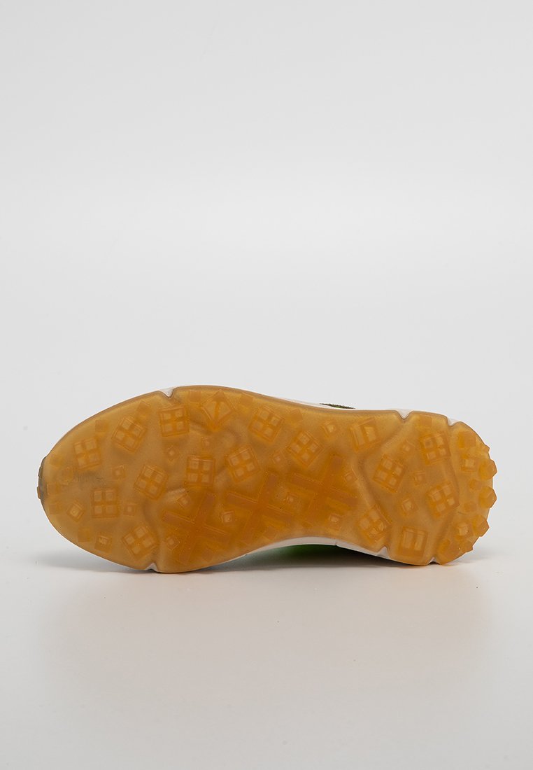 La suela del zapato presenta un material de goma texturizada con un patrón de pequeños cuadrados y triángulos, principalmente de color marrón-naranja, que muestra signos de desgaste.