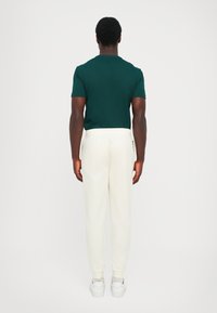 Men's outfit: dark green t-shirt, white elastic waistband joggers with side pockets, and white sneakers. Simple, fitted design.