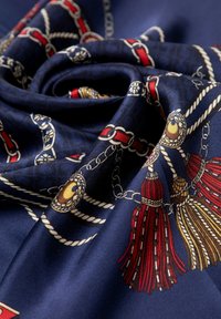 Bufanda de seda azul marino con cadenas doradas y flecos rojos, adornada con patrones intrincados. La tela tiene una textura suave y una profundidad de color rica.