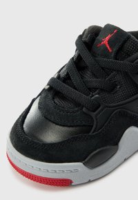 Chaussure de sport noire avec un mélange de daim texturé et de cuir lisse, avec des accents rouges, des lacets et une semelle en caoutchouc grise.
