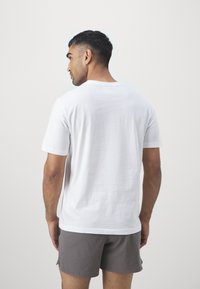 Vit bomulls t-shirt med kort ärm och rund halsringning, bärs med grå shorts; enkel design, tydlig textur synlig.
