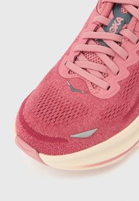Ροζ αθλητικό παπούτσι με υφασμάτινο άνω μέρος με υφή, κορδόνια στο ίδιο χρώμα και ελαφριά λαστιχένια σόλα με έντονη λογότυπο και ασημένιες λεπτομέρειες.