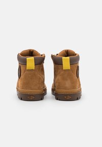 Stivaletti alla caviglia in suede marrone con un inserto giallo, dettagli marroni scuri e suole in gomma con un logo distintivo sul tallone.