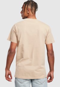 Béžové bavlněné tričko s krátkým rukávem, rovného střihu a bezšvým výstřihem. Materiál vypadá hladce s minimalistickým designem.