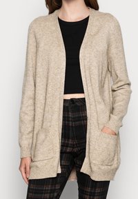 Cardigan beige lavorato a maglia con apertura frontale, maniche lunghe e due tasche frontali. Presenta polsini e orlo a costine, una texture morbida e una vestibilità rilassata.