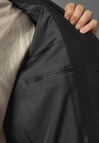 Sacou negru cu căptușeală netedă, având un buzunar elegant pe partea stângă. Materialul are o textură moale.