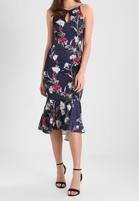Abito floreale navy con design senza maniche, scollatura a chiave e orlo svasato. Presenta pois bianchi e motivi floreali vivaci in rosso e bianco.