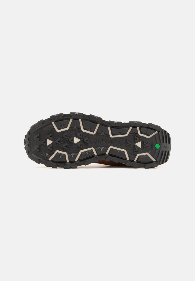 Semelle en caoutchouc avec des motifs profonds, présentant un mélange de couleurs noir et beige. Motif de traction géométrique notable avec une touche de vert.