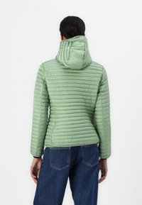 Lys grøn pufferjakke med hætte, ribbet tekstur, designet med vandret syninger, parret med blå jeans.
