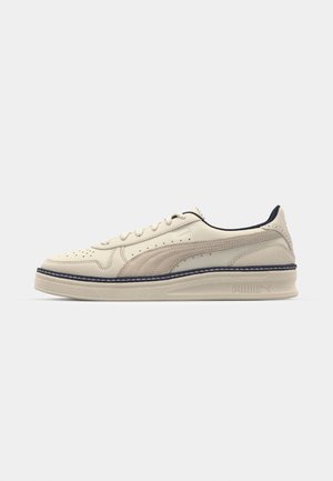 Baskets beige avec une tige en cuir texturé, des accents perforés, des coutures bleu marin et une semelle en caoutchouc. Présente un logo discret sur le talon.