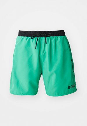 Roheline ujumispüksid, mis on valmistatud kergest kangast, musta elastse vöökoha, paelaga ja küljetaskutega. Bränding põhiküljel.