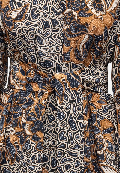 Καφέ, μαύρο και λευκό ύφασμα με ανθισμένο και αφηρημένο σχέδιο και δεμένη ζώνη στη μέση ενός ενδύματος.