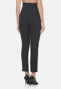 Pantaloni neri a vita alta con un design aderente, caratterizzati da inserti lucidi sui lati e gamba affusolata, abbinati a scarpe nere con tacchi alti.