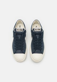 Zapatillas Converse All Star de color azul marino, con parte superior de ante y lona, suela de goma blanca, punta redonda y cordones en un tono similar. Diseño casual, estilo clásico.
