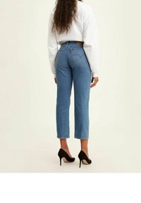 Jeans di denim blu a vita alta con cuciture visibili sulle tasche, modello a gamba dritta, orlo sfrangiato e patch del marchio in pelle marrone sul retro.