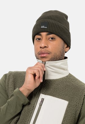 Berretto a coste verde oliva con patch logo nero, indossato con un gilet in pile con zip, caratterizzato da un pannello bianco e una superficie testurizzata.