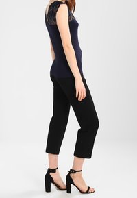 Námořnický bezrukávový top s krajkovými detaily na ramenech, spárovaný s černými zkrácenými kalhotami a černými sandály na podpatku s pásky kolem kotníků.