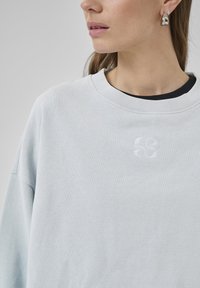 Felpa azzurra chiara con scollo rotondo, vestibilità comoda e logo ricamato sul petto. Tessuto morbido e dettagli di cucitura delicati.