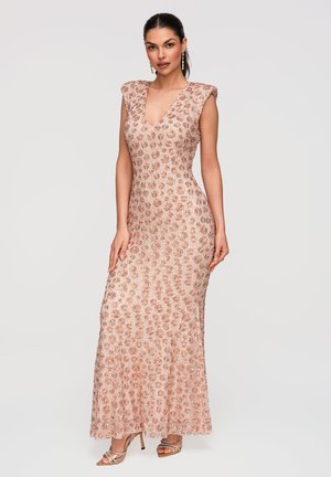 Kvinde iført ærmeløs kjole med lyserød guldpalietter og dyb V-udskæring, kombineret med sandaler med stropper og høje hæle samt hængende øreringe.